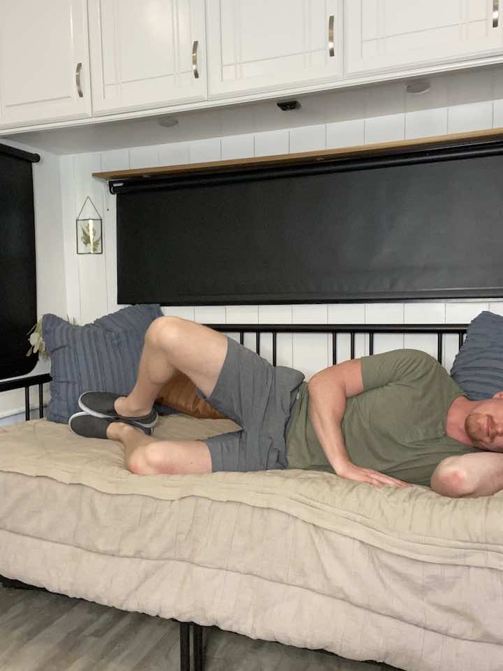 Knee Pain Specialist and Injury Prevention Expert, Coach Todd, lying on his side with knees bent and lifting his top knee, demonstrating clamshell exercises