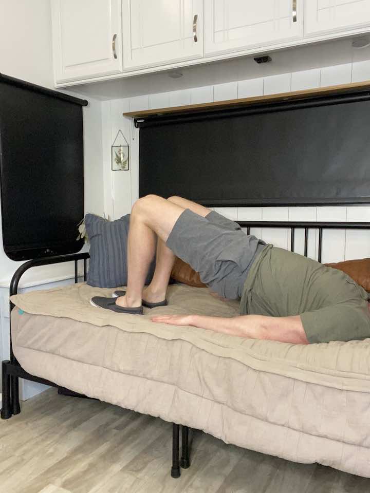 Knee Pain Specialist and Injury Prevention Expert, Coach Todd, lying on his back with knees bent and lifting his hips off the ground, demonstrating bridge exercises for lumbar stabilization.