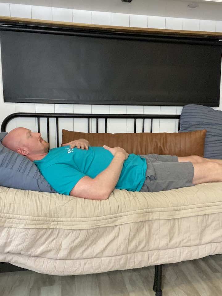 Knee Pain Specialist and Injury Prevention Expert, Coach Todd, lying on his back with hands on his stomach, demonstrating diaphragmatic breathing exercises for lumbar stabilization.