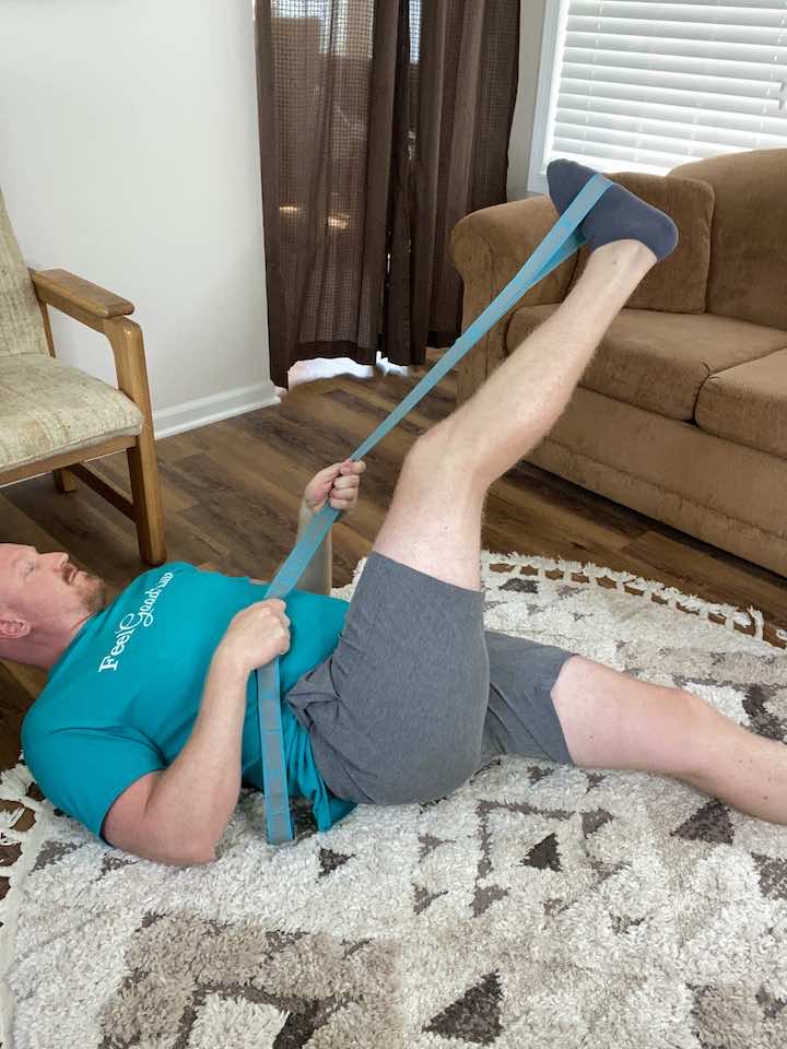 Coach Todd demonstrating the IT Band Stretch lying on the back using a rope, an effective stretch to alleviate pain associated with iliotibial band syndrome.