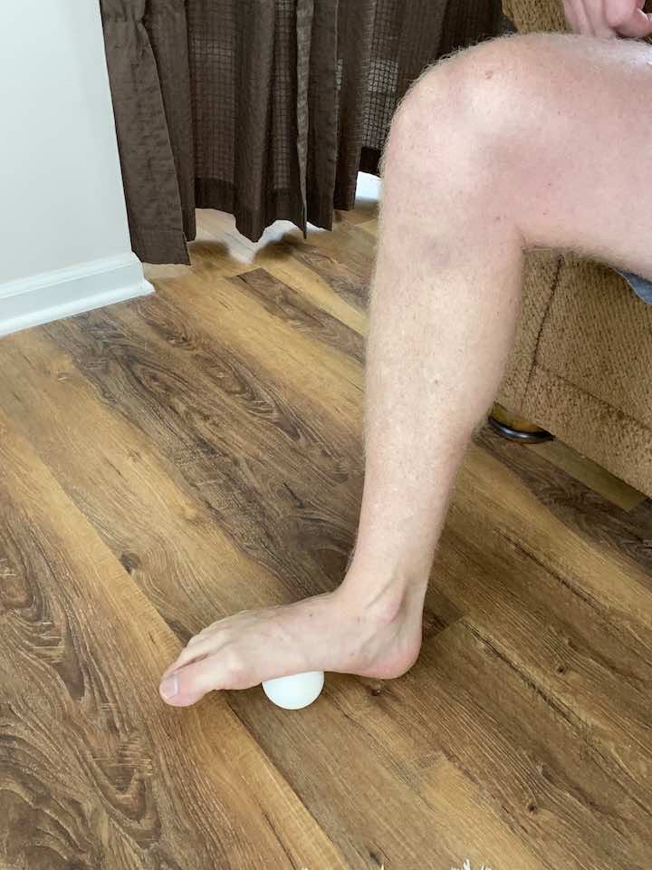 Performing plantar fasciitis golf ball rollout, a therapeutic exercise for relieving heel pain caused by plantar fasciitis.