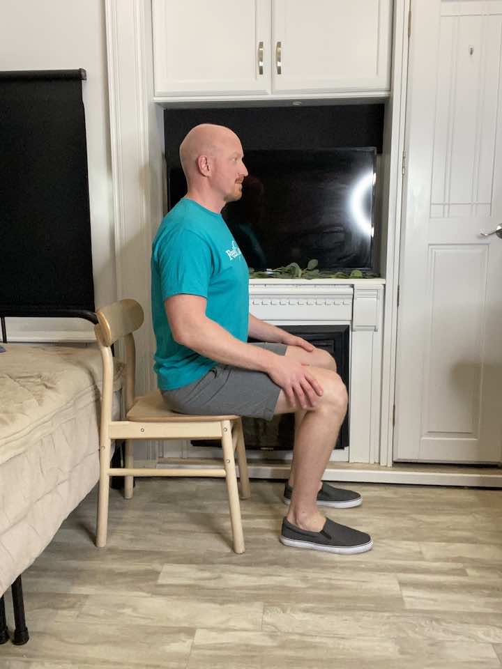 Engaging in seated cat/cow stretch, a chair-based variation to enhance lower back flexibility.